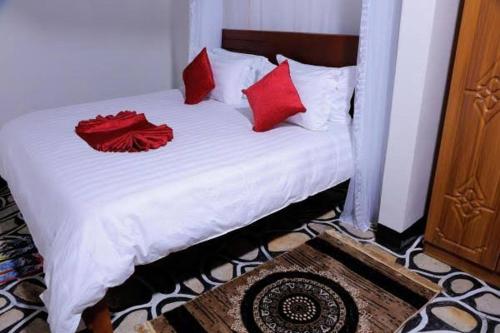 a white bed with red pillows on top of it at Margarita Safaris guest house in Kasese