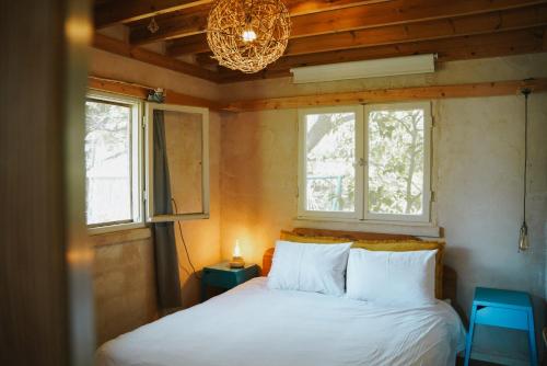 a bedroom with a bed with a chandelier and two windows at THE HOUSE IN THE OAKS הבית באלונים in Amirim