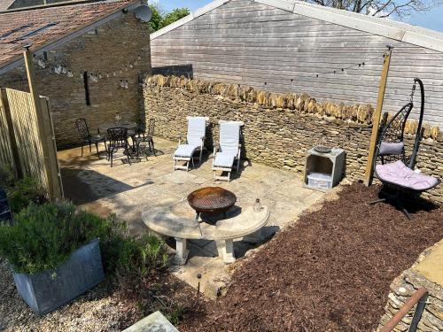 a patio with a fire pit and chairs and a brick wall at Paddock View, Castle Combe in Castle Combe