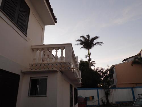 a white house with a balcony and a palm tree at Pousada Casa dos Sonhos in Rio das Ostras