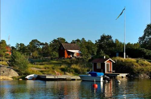 a small house and a boat on a body of water at Cabin retreat in the archipelago in Djurhamn