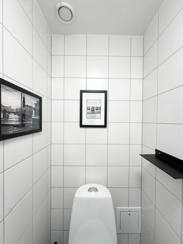a white tiled bathroom with a toilet and a tv at Linnéplatsens Hotell & Vandrarhem in Gothenburg