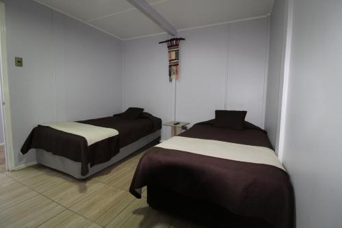 two beds in a room with white walls at Juku Hostal in Calama