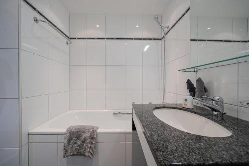 a white bathroom with a sink and a tub at Galerie Obersee 4C in Arosa