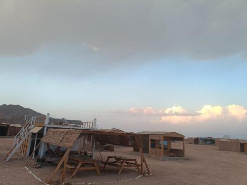 a shack with a table and a bench on a beach at Sea sound Camp in Nuweiba‘ el Muzeinah