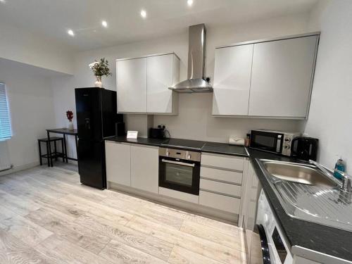a kitchen with white cabinets and a black refrigerator at Modern Boutique Apartment Great Location in Golders Green