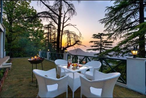een witte tafel en stoelen op een balkon met uitzicht op de zonsondergang bij HOTEL THE PINE VILLA MUSSOORIE in Mussoorie
