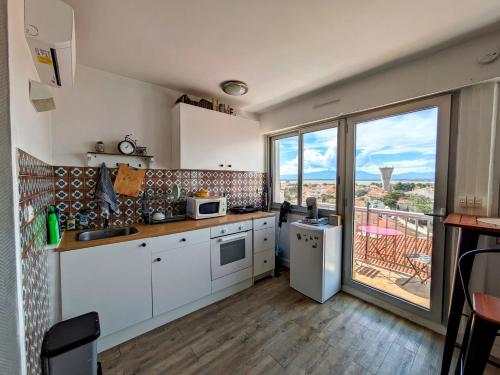 une cuisine avec des placards blancs et une grande fenêtre dans l'établissement Studio cosy en front de mer avec belle vue panoramique sur les montagnes, à Canet