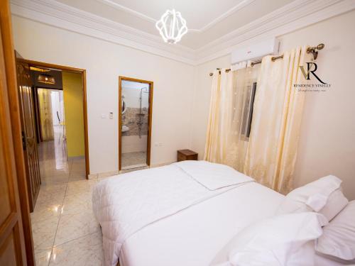 a bedroom with a white bed and a mirror at Résidence Vinelly in Douala