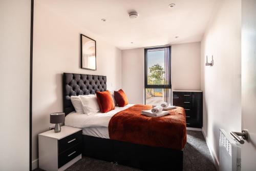 1 dormitorio con 1 cama con almohadas de color naranja y ventana en Modern 3 Bedroom Manchester Apartment, en Mánchester