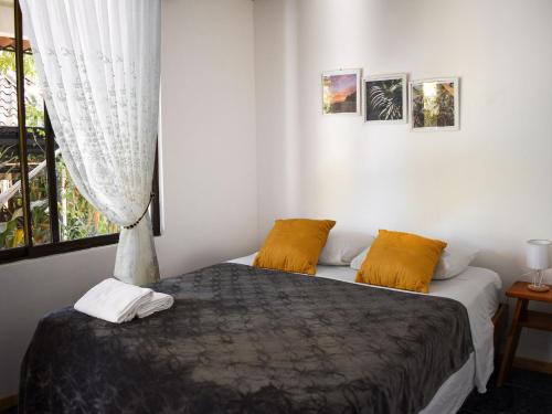 een slaapkamer met een bed met gele kussens en een raam bij La Posada - Hostel in Santa Teresa Beach
