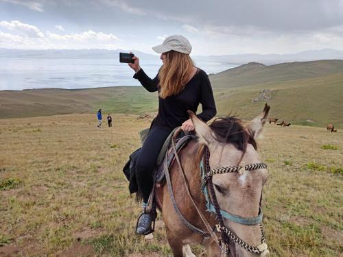 a woman riding a horse while taking a picture at Song Kol lake, Flex Travel yurt camp, horse riding in Song-Kul