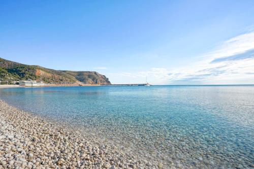 a beach with blue water and a rocky shore at Solmar Javea in Jávea
