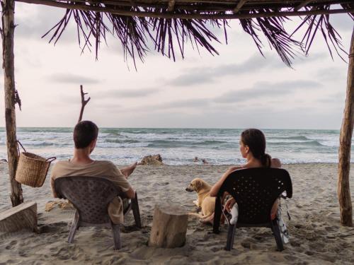 a couple sitting on the beach with their dog at Paraíso Natural Ecohotel in San Bernardo del Viento