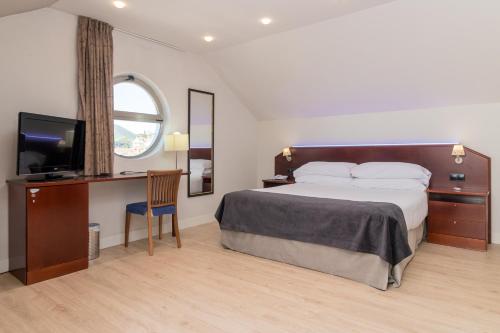 a bedroom with a bed and a desk with a television at Hotel Milagros Golf in Mogro