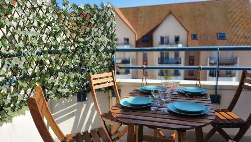 une table en bois avec des assiettes et des verres sur un balcon dans l'établissement Le clos des Boucaniers, à Berck-sur-Mer