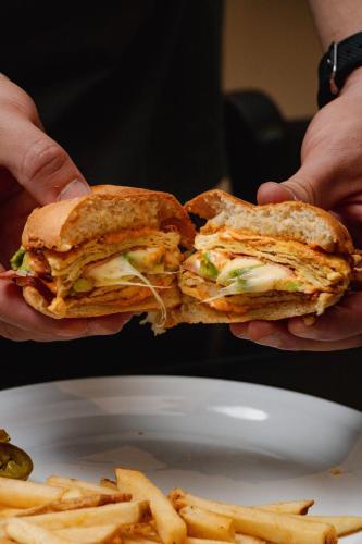 two hands holding a sandwich and french fries on a plate at Hotel Maioris El Diez Culiacan in Culiacán
