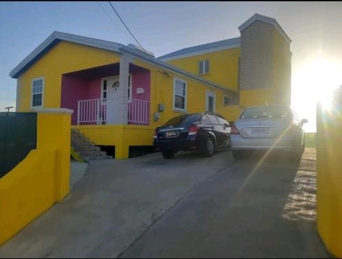 uma casa amarela com dois carros estacionados em frente em Fabulous Apartments Barbados em Christ Church