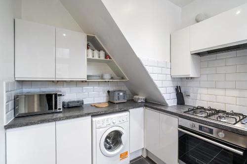 a kitchen with white cabinets and a washer and dryer at Modern 3 bedroom apartment in Wimbeldon Park in London