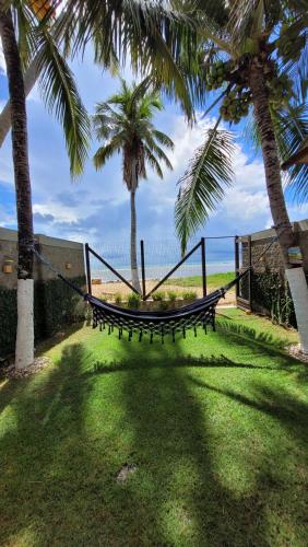 a hammock in a yard with palm trees and the ocean at Casa à beira mar de Maragogi com 3 quartos, 4 banheiros e Área Verde in Maragogi