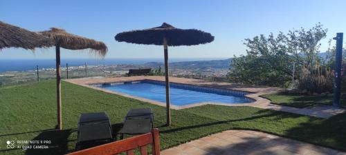 uma piscina com duas cadeiras e guarda-sóis em Refugio del Mirador em Vélez-Málaga
