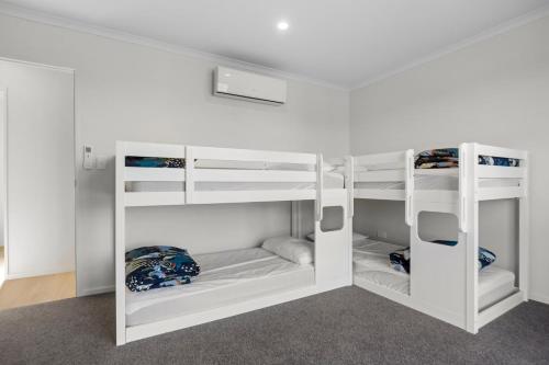 a bunk bed with white bunk beds in a room at Modern Family Bach - Waihi Beach Holiday Home in Waihi