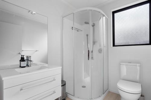 a white bathroom with a shower and a toilet at Modern Family Bach - Waihi Beach Holiday Home in Waihi