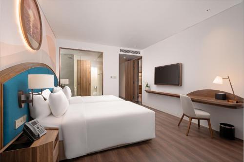 a hotel room with a large white bed and a desk at Wyndham Garden Sonasea Van Don in Cái Rồng