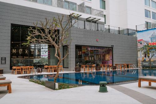 a building with a swimming pool and tables and chairs at Moxy Bengaluru Airport Prestige Tech Cloud in Devanahalli-Bangalore