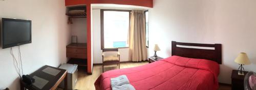 a bedroom with a red bed and a television at Hostal El Candelabro in Pisco