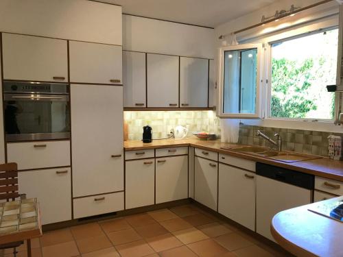 cocina con armarios blancos, fregadero y ventana en 2 chambres adjacentes dans villa avec jardin de pins en Commugny
