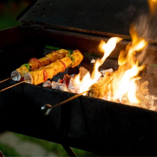 a bunch of food cooking on a grill with flames at ELIVAAS 6 BHK Farmhouse with Pvt Pool & Garden - Enchantia in Bhundsi