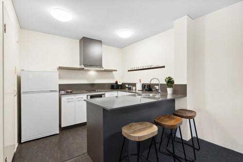 a kitchen with white cabinets and a counter with stools at Spacious Holiday Apart on Hay St CBD in Perth