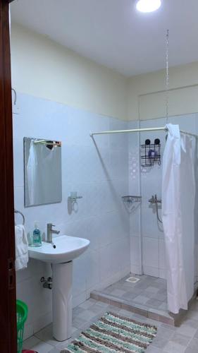 La salle de bains blanche est pourvue d'un lavabo et d'une douche. dans l'établissement Haz Furnished Apartments Buwate, à Kampala