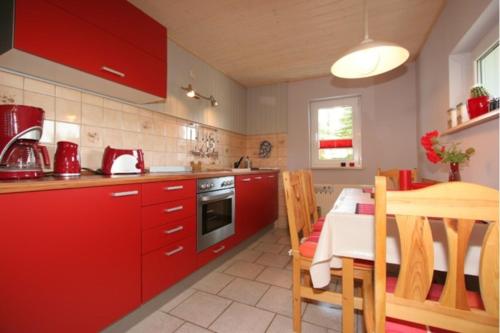 uma cozinha com armários vermelhos, uma mesa e uma sala de jantar em Ferienhaus Eulennest - Ulenhoef em Prerow