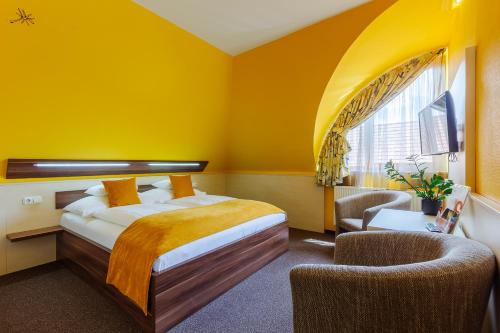a bedroom with yellow walls and a bed and a chair at Hotel Mayer Alsóörs in Alsóörs