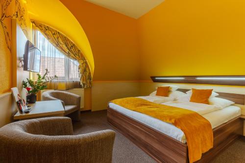 a bedroom with orange walls and a bed and a chair at Hotel Mayer Alsóörs in Alsóörs