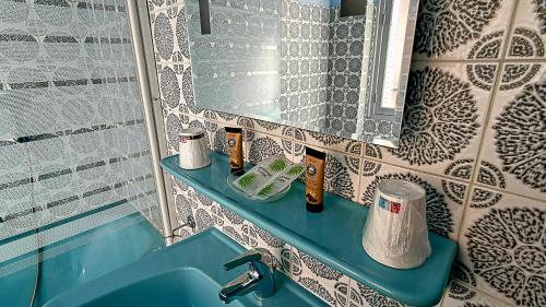 La salle de bains est pourvue d'un lavabo bleu et d'un miroir. dans l'établissement Trianon, à Vichy