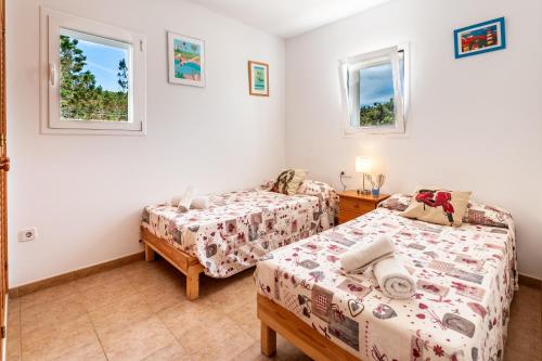 a bedroom with two beds and two windows at Casa Es Vedrà in Cala Saona