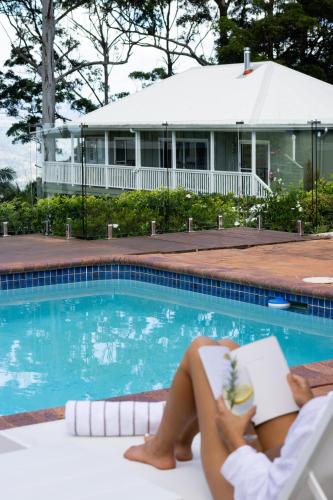 a woman reading a book next to a swimming pool at Verandah House Country Estate in Mount Tamborine