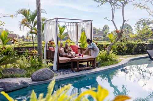 una pareja sentada en un columpio junto a la piscina en un complejo en Candy Villa by Pramana Villas en Ubud