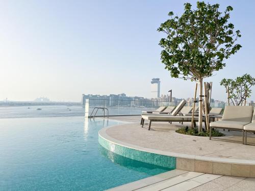 a pool with lounge chairs and a tree next to the water at 2BR Beachfront Gem with Dazzling Views of the Palm in Dubai