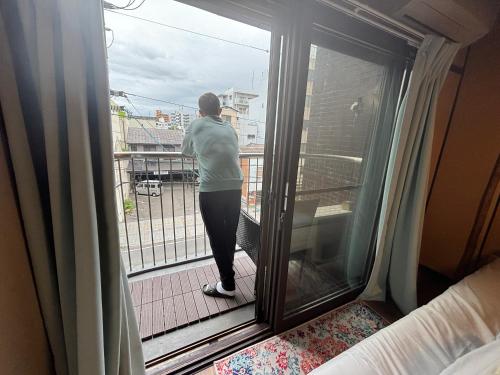 a woman standing on a balcony looking out the window at 777 Takamatsu Guest House in Takamatsu