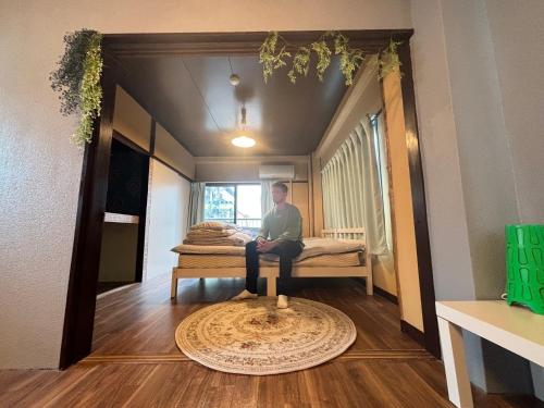a man sitting on a bed in a room at 777 Takamatsu Guest House in Takamatsu