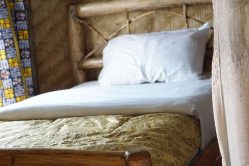 a bed with a wooden headboard and white pillows at FRAMA ECO LODGE, Twin Lakes (big island)- Lake Burera 
