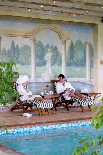 two people sitting in lounge chairs next to a swimming pool at Coach House Hotel & Spa Tzaneen in Tzaneen