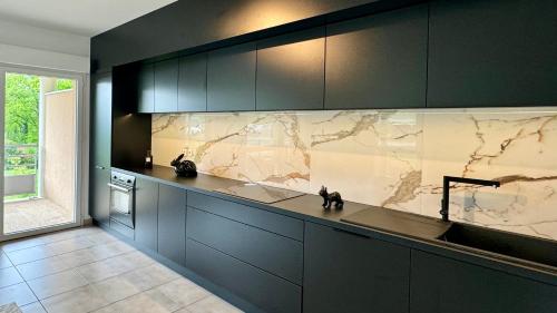 - une cuisine avec des placards noirs et un mur en marbre dans l'établissement La maison de Louise à 10 min Genève, à Vétraz-Monthoux