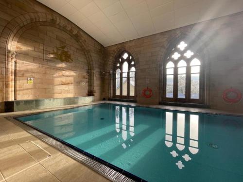 uma grande piscina num grande quarto com janelas em The Classrooms, Loch Ness Abbey - 142m2 Lifestyle & Heritage apartment - Pool & Spa - The Highland Club - Resort on lake shores em Fort Augustus