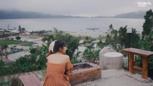 a woman standing on a ledge looking out at the water at Puncak Lestari Villa Bedugul by BIJAK in Bedugul