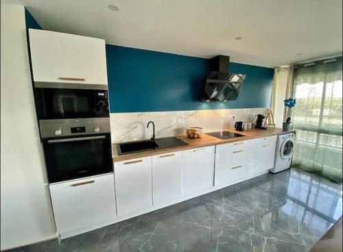 a kitchen with white cabinets and a blue wall at L’élégant cosy in Cournon-dʼAuvergne